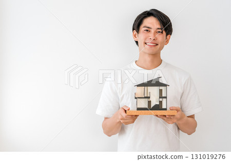 微笑的年輕亞洲男子拿著房屋模型（我的家、獨立式住宅、住宅建築） 131019276