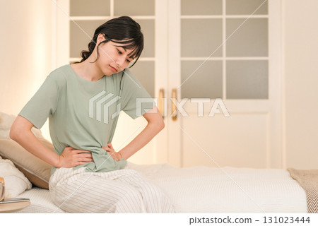Young Asian woman suffering from abdominal pain and menstrual cramps in her bedroom at night Young Asian woman suffering from abdominal pain and menstrual cramps in her bedroom at night 131023444