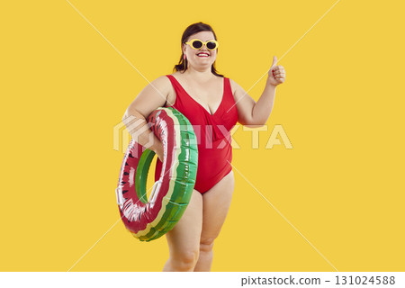 Fat woman in rubber ring wearing swimsuit showing thumb up sign on yellow background. Fat woman in rubber ring wearing swimsuit showing thumb up sign on yellow background. 131024588