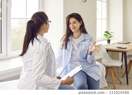 Doctor holding report file with appointment and listening her woman patient in clinic. 131024589