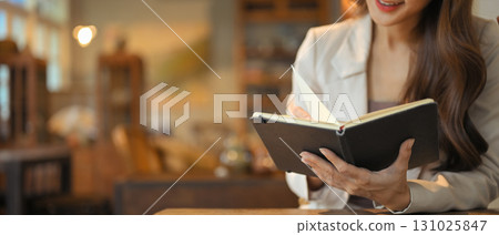 A woman is sitting at a daily book with a book in her hand A woman is sitting at a daily book with a book in her hand 131025847