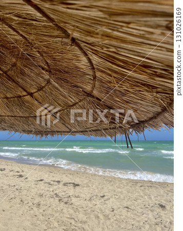 Enjoying a peaceful day at the blue waves of Djerba beach under a straw parasol Enjoying a peaceful day at the blue waves of Djerba beach under a straw parasol 131026169