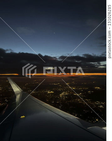 Sunset view from an airplane wing displaying the sky, clouds, and city lights in the distance near Sunset view from an airplane wing displaying the sky, clouds, and city lights in the distance near 131026285