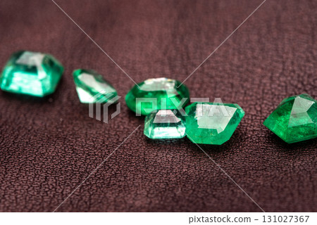 A bunch of green gemstones are on a dark surface 131027367