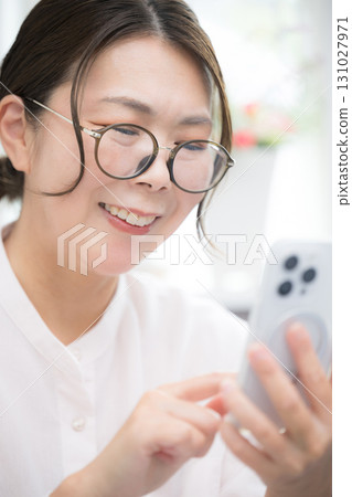 Close-up of the upper body of a woman in her 40s tapping on a smartphone in a room 131027971