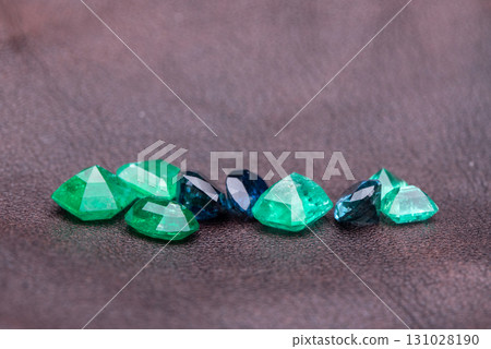 A collection of green, blue, and black gemstones are laid out on a dark surface 131028190