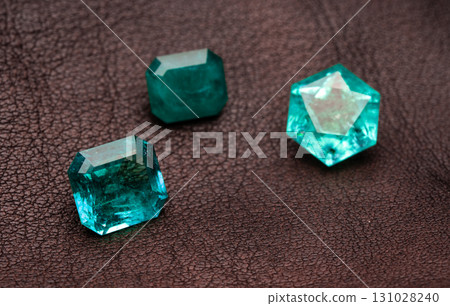 Three green gemstones are on a brown surface Three green gemstones are on a brown surface 131028240
