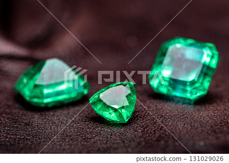 Three green gemstones are displayed on a dark surface Three green gemstones are displayed on a dark surface 131029026