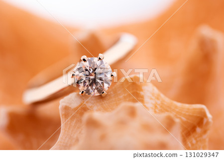 A diamond ring is set in a gold band and is resting on a shell 131029347