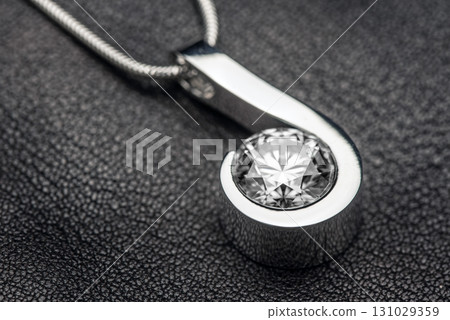 A silver and white diamond pendant is displayed on a black surface 131029359