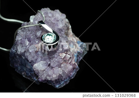 A necklace with a large crystal pendant sits on a purple rock 131029368