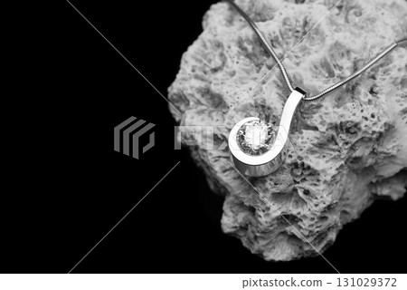 A silver necklace with a diamond pendant is on a rock 131029372