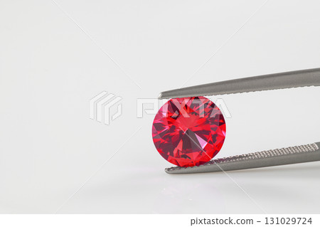 A red gemstone is being held up by a metal tool 131029724