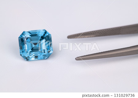 A blue gemstone is on a table next to a pair of tongs 131029736