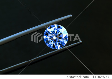 A blue diamond is being held up by a pair of tweezers A blue diamond is being held up by a pair of tweezers 131029747