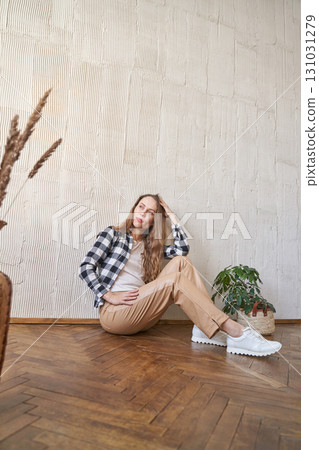 Young caucasian female sitting on floor in casual outfit with indoor plant 131031279
