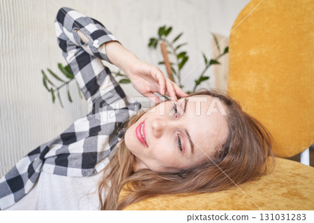 Relaxed young caucasian female lying on yellow chair at home listening to music Relaxed young caucasian female lying on yellow chair at home listening to music 131031283