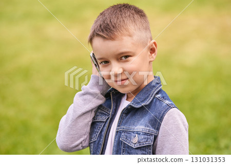Caucasian young male child smiling outdoors in denim vest talking on smartphone Caucasian young male child smiling outdoors in denim vest talking on smartphone 131031353