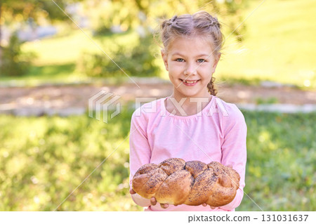 Caucasian young girl holding freshly baked bread outdoors in sunny park 131031637