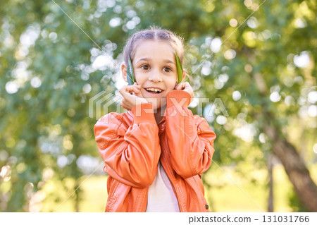 Happy caucasian girl in orange jacket enjoying nature in park surrounded 131031766