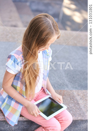 Caucasian young girl with long hair using tablet outdoors on stone steps Caucasian young girl with long hair using tablet outdoors on stone steps 131031801