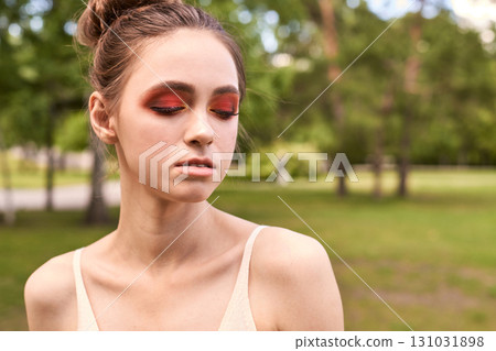 Young caucasian female with red eye makeup in outdoor park setting Young caucasian female with red eye makeup in outdoor park setting 131031898