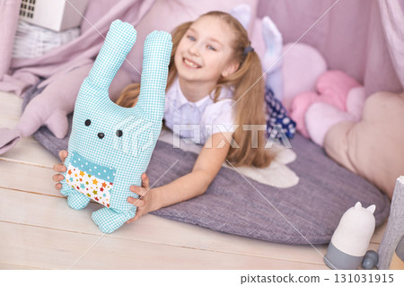 Caucasian young girl playing indoors with blue plush toy in cozy tent 131031915