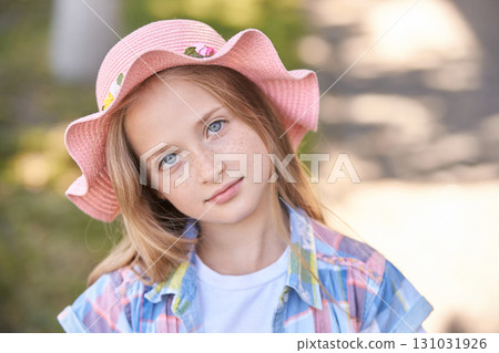 Caucasian young girl with freckles wearing a pink hat in park setting 131031926