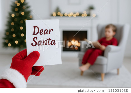 Santa claus gloved hand holding letter with child reading by fireplace in christmas decor concept of holiday spirit warmth cozy winter scene 131031988