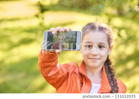 Young caucasian female child taking selfie in orange jacket outdoors 131032035