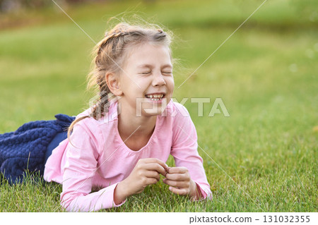 Caucasian young girl lying on grass smiling with eyes closed in pink shirt 131032355
