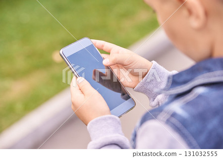 Young caucasian male child using smartphone outdoors in a denim jacket 131032555