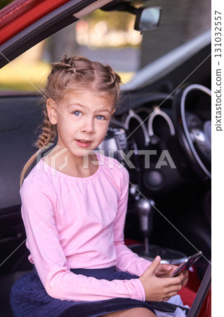 Blonde caucasian young girl with braids sitting in car holding phone 131032557