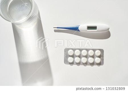 Digital thermometer, glass of water, and blister pack of pills on white surface 131032809