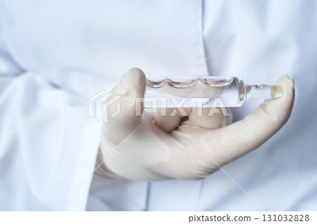 Gloved hand holding glass syringe by caucasian female adult in lab coat Gloved hand holding glass syringe by caucasian female adult in lab coat 131032828