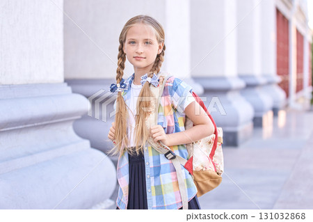 Caucasian female child with braids and backpack standing outdoors at school Caucasian female child with braids and backpack standing outdoors at school 131032868