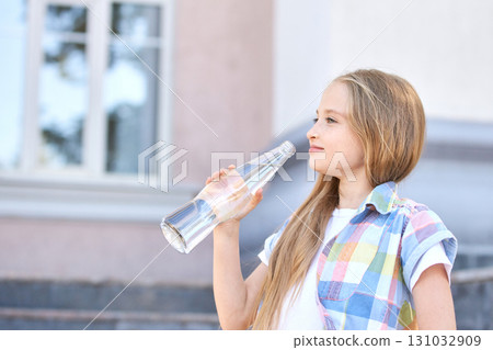 Young caucasian girl drinking water outdoors with a clear bottle on a sunny day 131032909