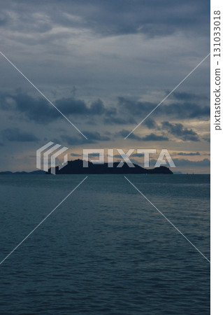 Serene evening seascape with distant island under cloudy sky reflecting in calm Serene evening seascape with distant island under cloudy sky reflecting in calm 131033018