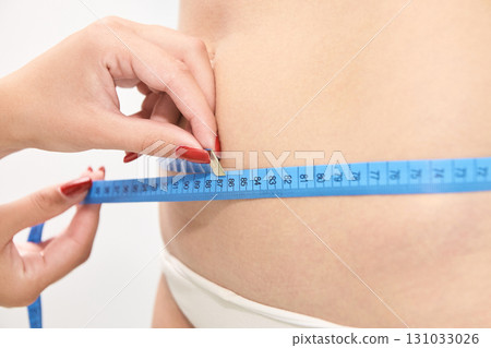 Female measuring waist with blue tape measure for fitness and health goals Female measuring waist with blue tape measure for fitness and health goals 131033026