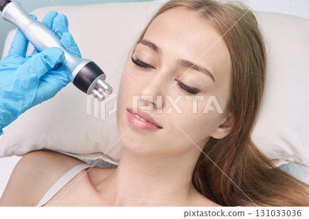 Young caucasian female receiving facial treatment in a beauty clinic by gloved Young caucasian female receiving facial treatment in a beauty clinic by gloved 131033036
