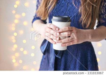 Young caucasian female in blue dress holding coffee cup with festive lights 131033067