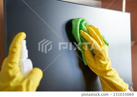 Person cleaning screen with green cloth and yellow gloves spray bottle indoors Person cleaning screen with green cloth and yellow gloves spray bottle indoors 131033069