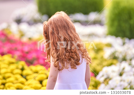 Young caucasian female child with curly hair in garden of colorful flowers Young caucasian female child with curly hair in garden of colorful flowers 131033078