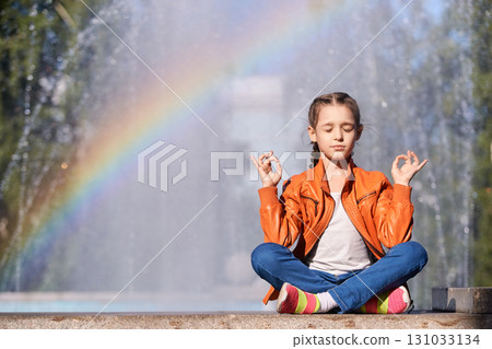Young caucasian girl meditating outdoors with rainbow in background near Young caucasian girl meditating outdoors with rainbow in background near 131033134