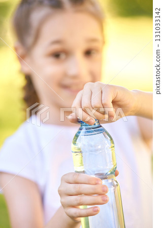 Caucasian young female child opening bottle of water outdoors on a sunny day Caucasian young female child opening bottle of water outdoors on a sunny day 131033142