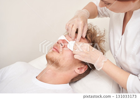 Young caucasian male receiving professional facial treatment with cotton pads 131033173
