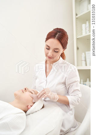 Young caucasian female aesthetician performing facial treatment on female client 131033180