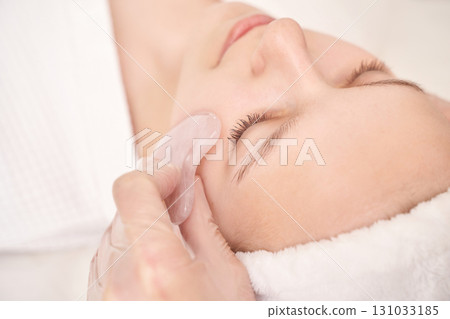 Young caucasian female enjoying relaxing facial massage with rose quartz gua Young caucasian female enjoying relaxing facial massage with rose quartz gua 131033185
