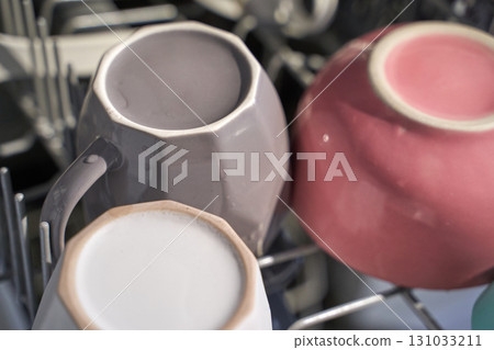 Three assorted ceramic coffee mugs in dishwasher rack with morning light 131033211