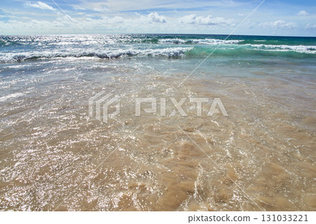 Serene ocean waves gently lapping at sandy beach on a sunny day with clear blue 131033221